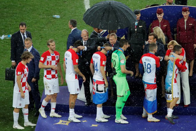 Medtem ko je bil ruski predsednik Vladimir Putin med podeljevanjem kolajn varno skrit pod dežnikom, sta bila hrvaška predsednica Kolinda Grabar Kitarović in francoski Emmanuel Macron – tako kot nogometaši – prepuščena na (ne)milost dežnih kapelj. FOTO: Reuters