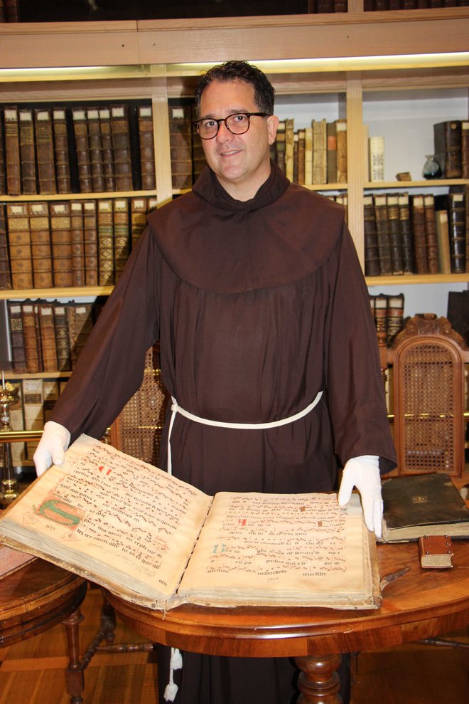 Gvardijan p. Tomaž Hočevar v samostanski knjižnici z najstarejšo knjigo iz leta 1418, ki so jo frančiškani prinesli iz Bosne.