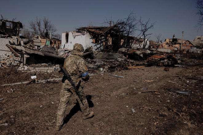 Ukrajinski vojak se sprehaja v vasi Malaja Roganj, ki je bila pred kratkim osvobojena ruskih sil. FOTO: Thomas Peter/Reuters
