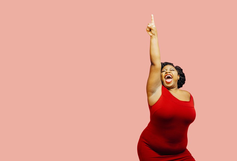 Fotografija: I did it! Portrait of a very happy and excited woman celebrating success with arm up, mouth open and finger pointing up, isolated on pink