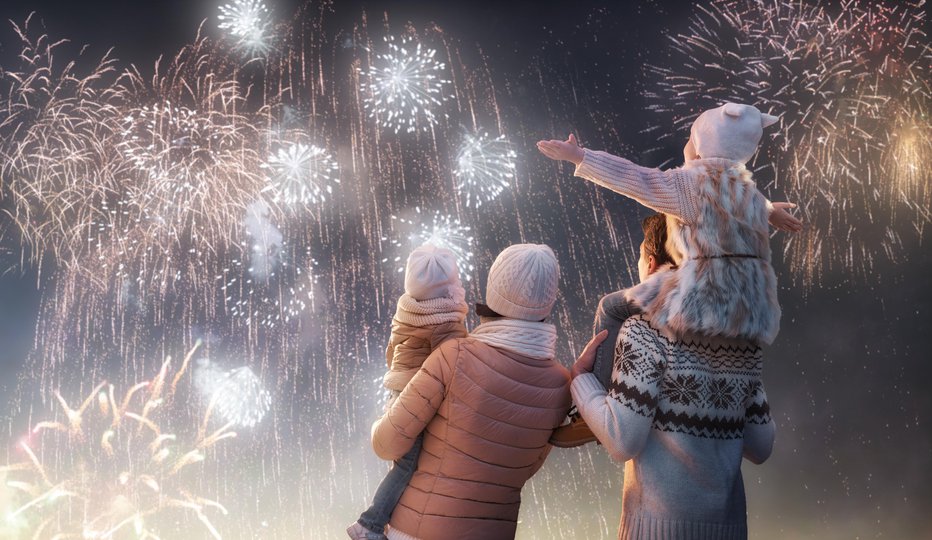 Fotografija: New Year holiday. Happy family, parents and daughters children girls are watching fireworks. The child sits on the shoulders of his father on snowy winter walk in nature. Holidays winter season.