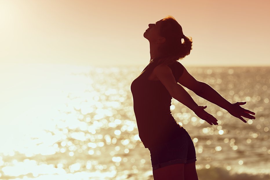 Fotografija: Woman relaxing in summer sunset sky at the beach, with open hands
