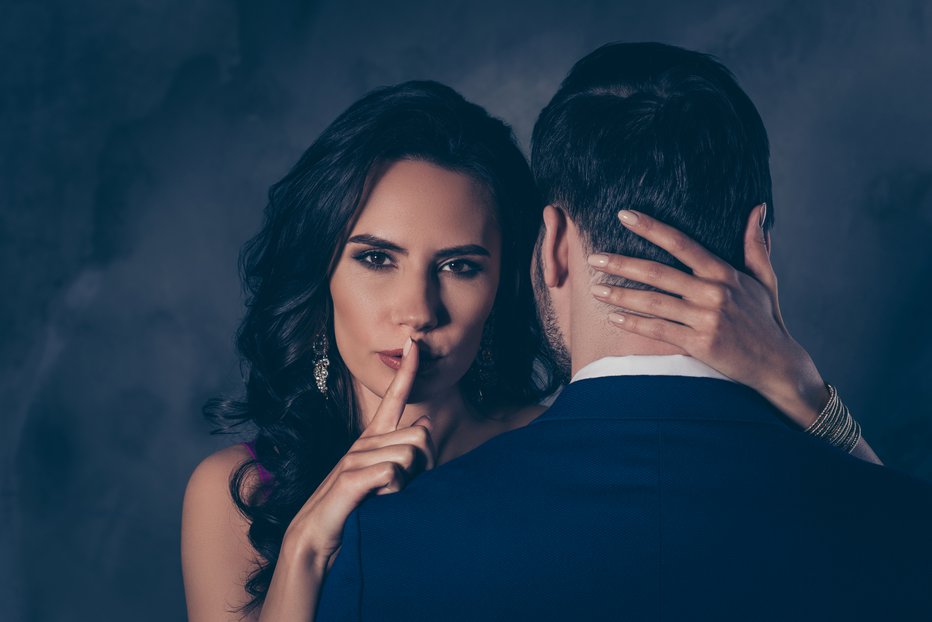 Fotografija: Shh! Portrait of tempting brunette lady showing silence sign with forefinger touching secret mysterious gentlemen with rear view, lovely Mr and Mrs isolated on grey background