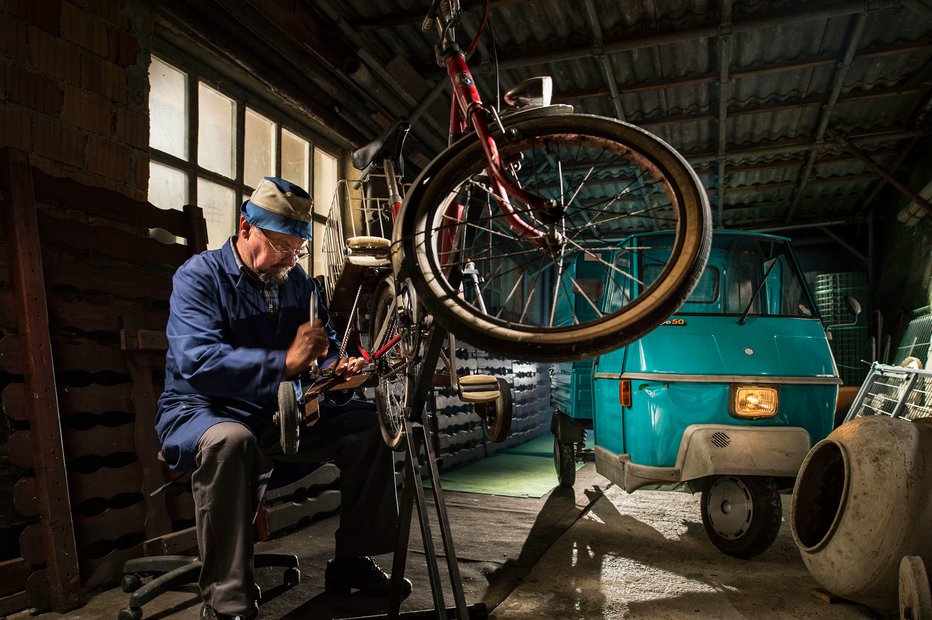 Fotografija: Kolesarski mehanik Lojze Recek pripravlja kolo za invalidko. Fotografije Branka Čeaka so znane po odlično izbrani svetlobi. FOTO: Branko Čeak