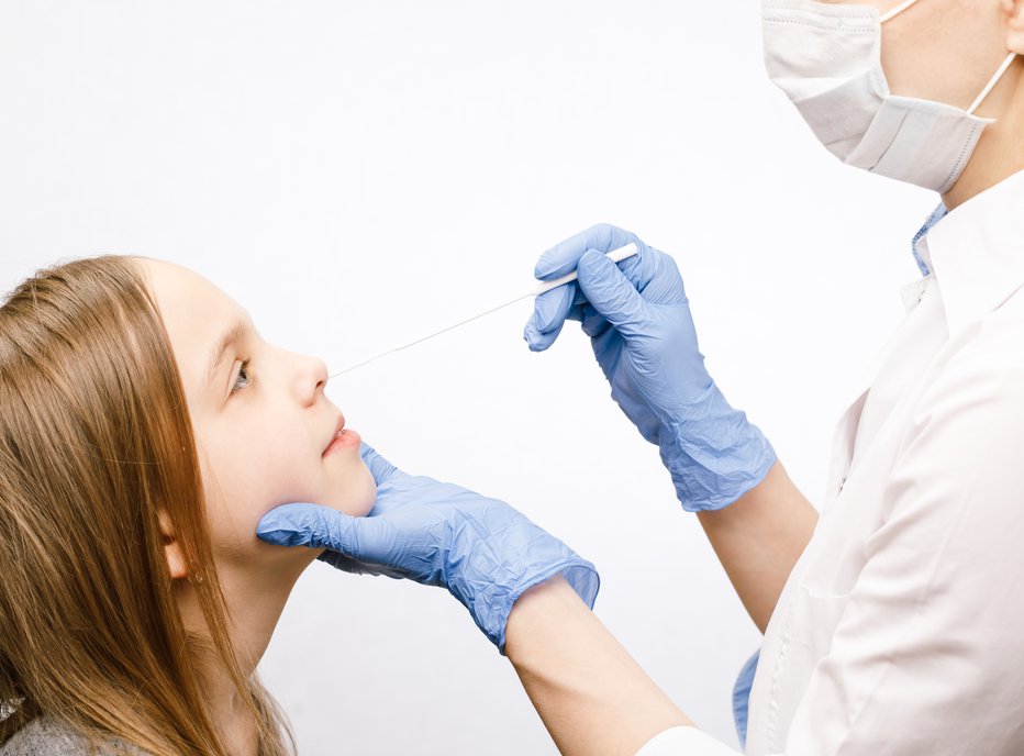 Fotografija: Pediatrician or doctor taking nasal mucus test sample from elementary age girl's nose performing respiratory virus testing procedure