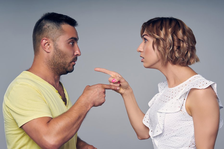 Fotografija: A couple man and woman pointing at each other expressing accusation isolated on gray background