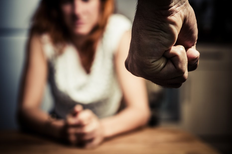 Fotografija: Young woman is sitting hunched at a table at home, the focus is on a man's fist in the foregound of the image