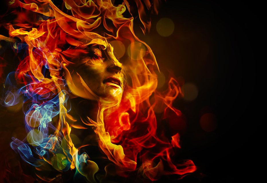 Fotografija: female face with closed eyes surounded by multicolored flames on a dark background

