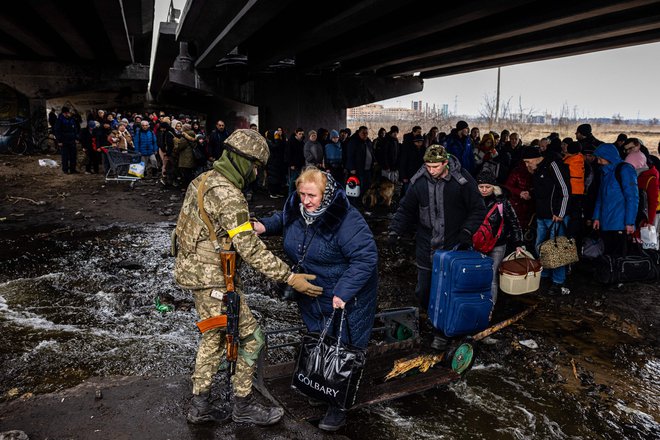 Ukrajinski uslužbenec pomaga evakuirancem, zbranim pod uničenim mostom, ko bežijo iz mesta Irpin, severozahodno od Kijeva. FOTO: Dimitar Dilkoff/Afp
