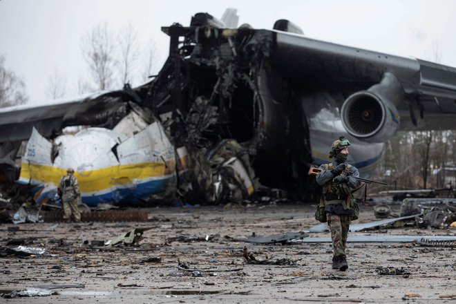 Ukrajinski pripadnik hodi pred tovornim letalom Antonov An-225 Mriya, največjim letalom na svetu, ki so ga uničile ruske čete med nadaljevanjem ruskega napada na Ukrajino, na letališču v Hostomelu. FOTO:Stringer/Reuters
