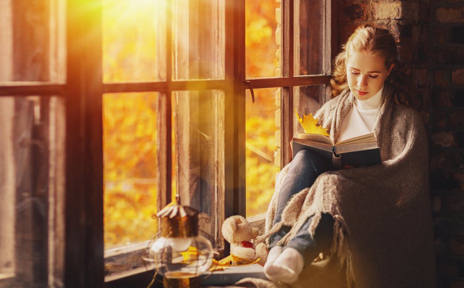 Fotografija: Happy young woman reading a book by the window in the fall