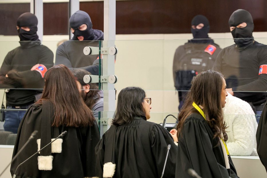 Fotografija: Zagovorniki v pogovoru z obtoženci, ki proces spremljajo v steklenih zabojnikih. Foto: Olivier Matthys/Reuters
