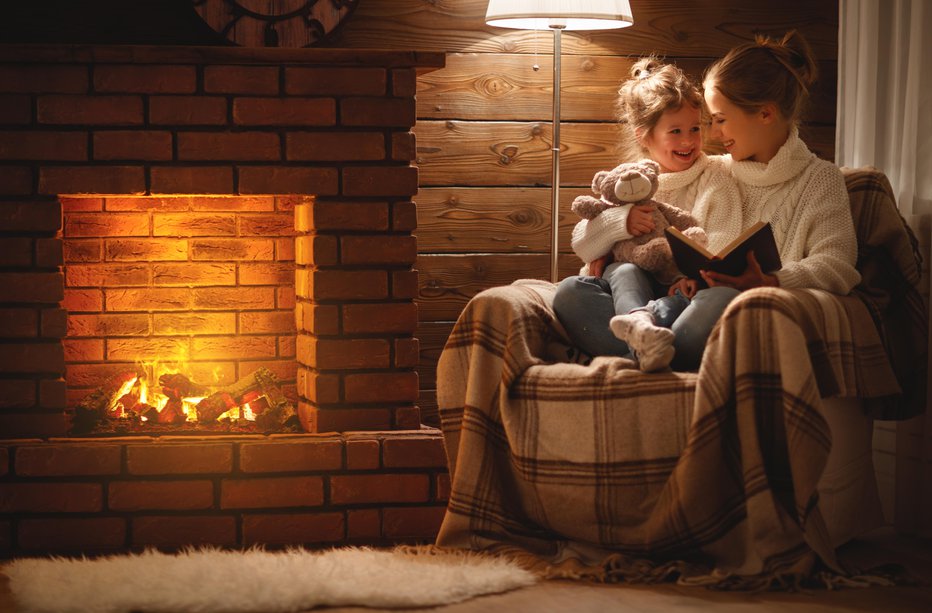 Fotografija: happy family mother and child daughter read a book on winter autumn evening near fireplace