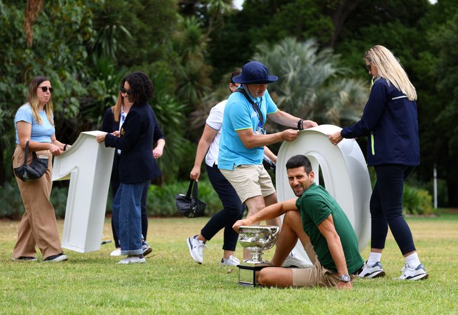 Prvak OP Avstralije Novak Đoković s pokalom, medtem ko osebje pripravlja prizorišče na fotografiranje.  FOTO: Hannah Mckay Reuters
