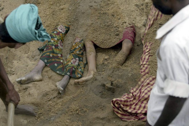 Vaščan pokriva trupla otrok, ki so bili ubiti v cunamiju v nedeljo na grobišču v Cuddaloreju, približno 185 km južno od Madrasa, v ponedeljek, 27. decembra 2004. Več kot 1000 ljudi je umrlo ob vzhodni obali Indije v nedeljo po močnem potresu ob indonezijskem otoku Sumatra sprožil ogromne plimne valove. Oblasti so povedale, da jih je na tisoče pogrešanih. Po neuradnih podatkih naj bi bilo žrtev 3000, je poročala televizija New Delhi. FOTO: Harish Tyagi, Reuters Pictures
