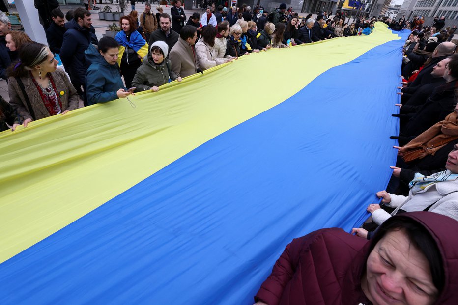 Fotografija: Ukrajinska zastava pred evropskim parlamentom v rokah podpornikov Ukrajine na dan obletnice ruskega napada. FOTO: Yves Herman Reuters
