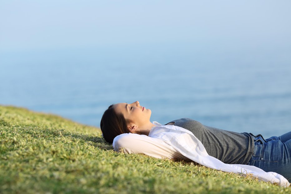 Fotografija: Side view portrait of a relaxed woman resting lying on the grass in the coast with the ocean in the background